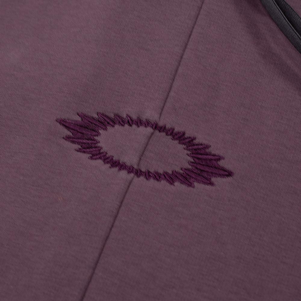 Macro perspective of the center chest embroidery on the Oakley FGL Slick Fleece Hoodie, focusing on the tonal deep violet thread forming a radiating, serrated outline of the Oakley Ellipse logo split by a clean vertical center seam.