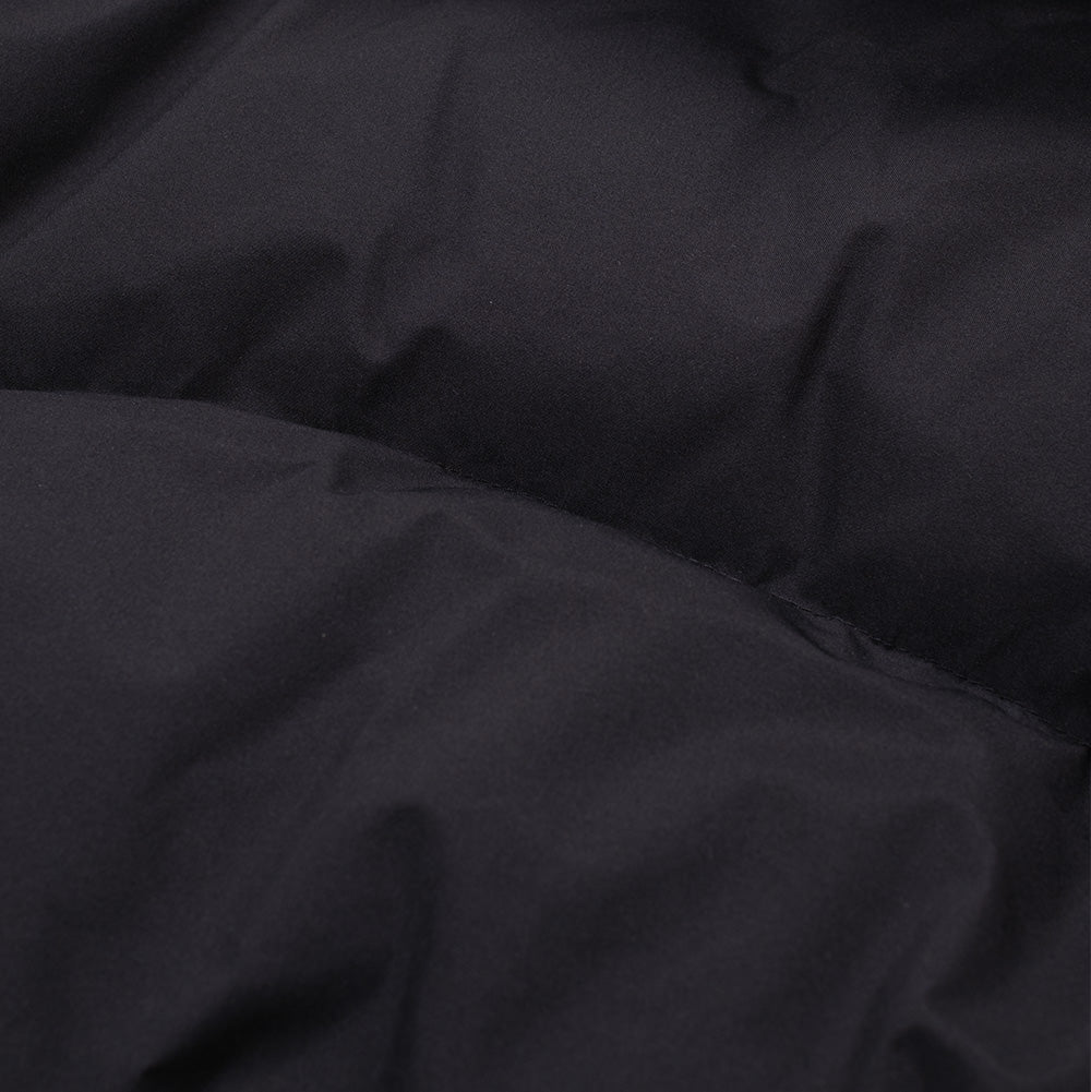 Macro perspective of the quilted exterior fabric on the Oakley Retrofuel Gore-Tex Down Jacket, emphasizing the smooth, matte surface texture of the weather-treated pitch black shell and the lofty loft of the down-filled insulation baffle.