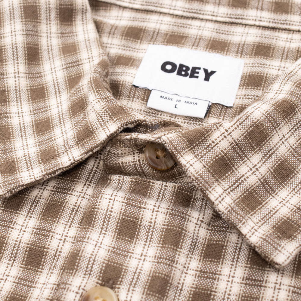 Macro studio close-up of the collar and upper buttons on the Obey Bigwig Axel Woven Shirt, highlighting the textured cotton twill weave, subtle brown marled button, clean collar stitching, and the white woven "OBEY" inner neck label.