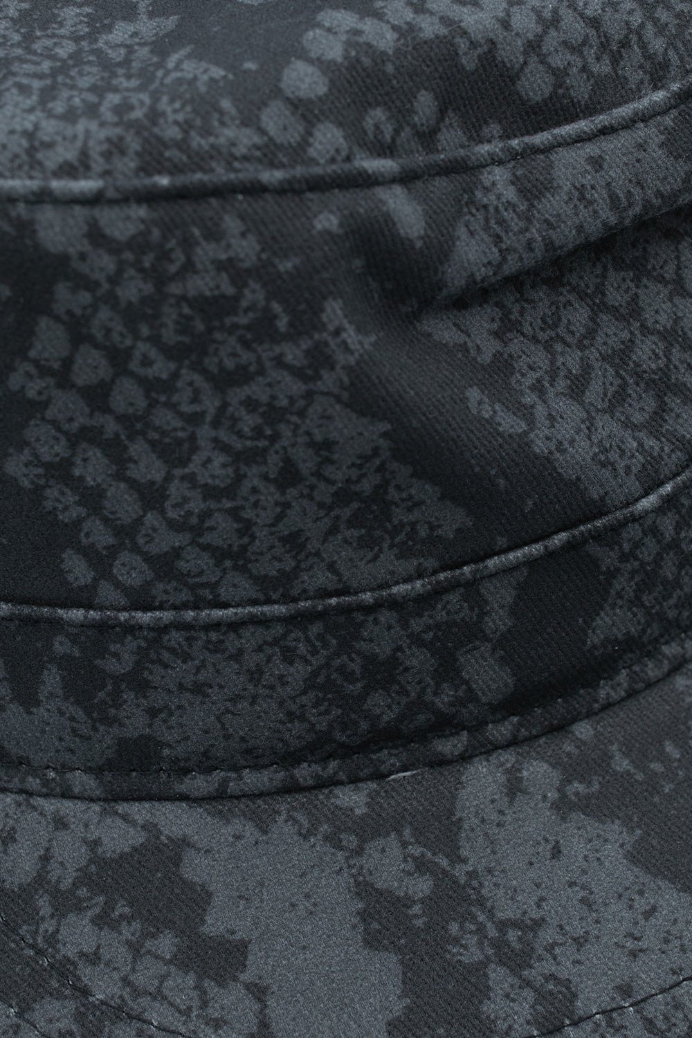 Macro detail shot of the crown and visor seam on the Obey Page Cadet Cap, showcasing the textured cotton twill weave printed with the intricate washed-out charcoal and black pigment snake skin scales alongside durable tonal topstitching.