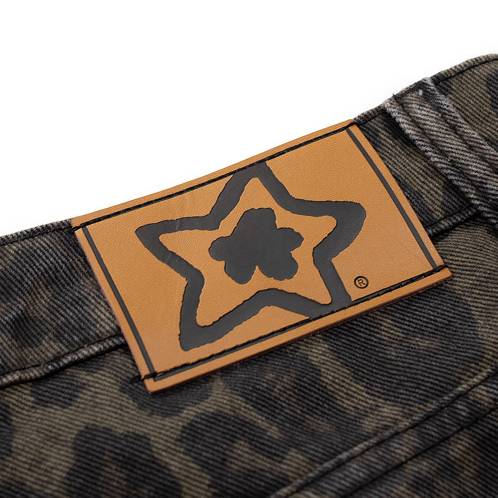 Macro studio shot of the rear waistband on the Starteam East Village Leopard Star Jeans, detailing the rectangular light cognac brown faux-leather jacron patch debossed with black Starteam flower-star brand artwork, stitched securely along the upper waist seam of the olive leopard denim pants.