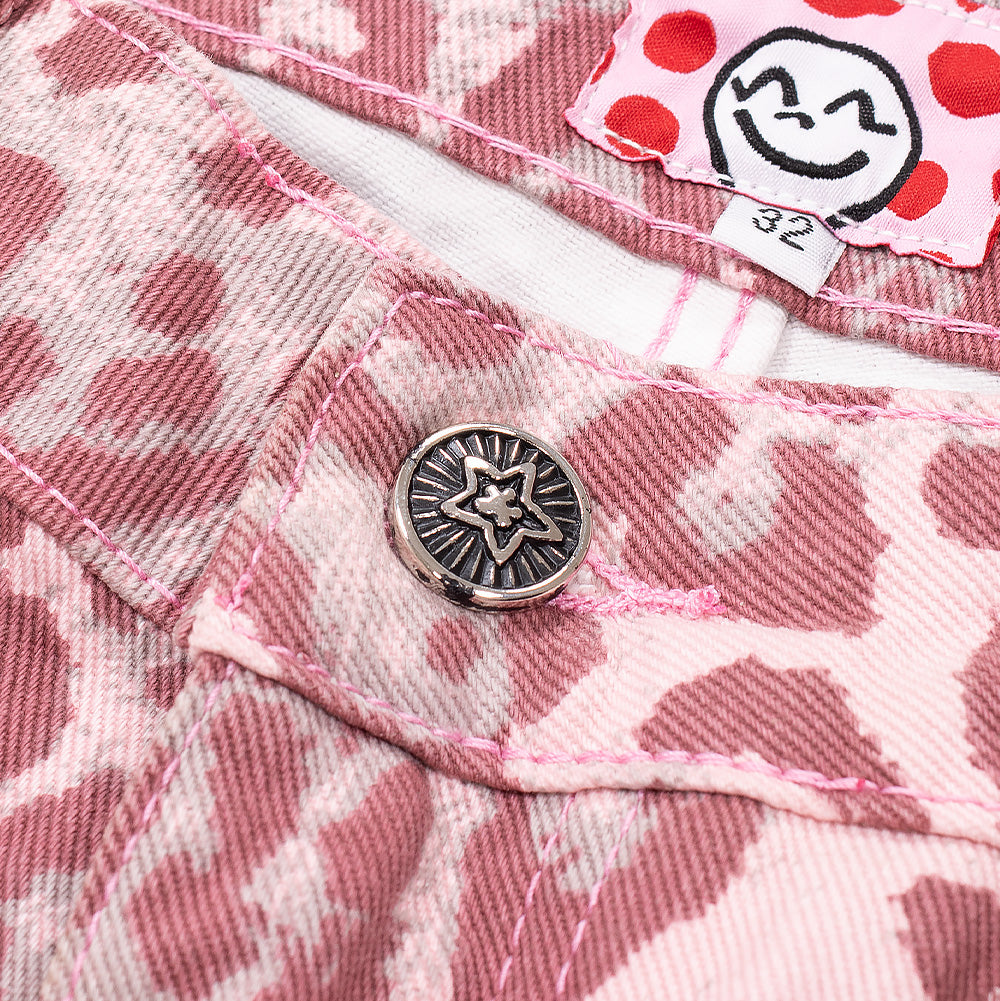 Detailed macro studio close-up of the front waistband closure on the Starteam Leopard Star Jeans in Pink, highlighting the antique silver metal tack button with a raised sunburst star emblem, stitched pink twill denim buttonhole, and glimpses of the playful interior white-and-red polka-dot waistband lining with a cartoon character tag.