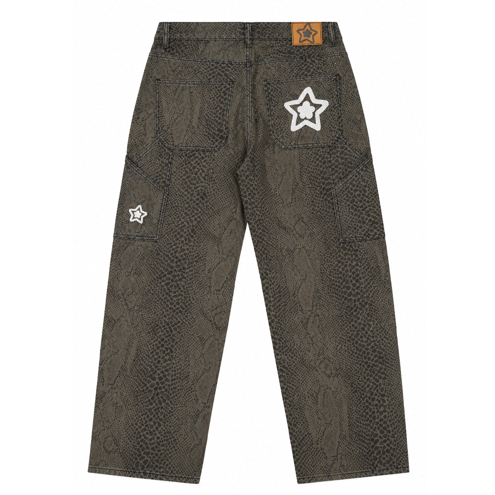 Back flat lay studio view of the Starteam East Village Snakeskin Star Jeans in washed olive green, presenting a wide straight-leg baggy skate silhouette constructed from heavyweight cotton denim covered in an intricate allover reptilian snakeskin scale print, equipped with dual utility carpenter pockets on the sides, an amber-brown faux-leather jacron patch on the waistband, and puffy white chain-stitched Starteam flower-star logo embroideries prominently displayed on the back right pocket and side leg pane