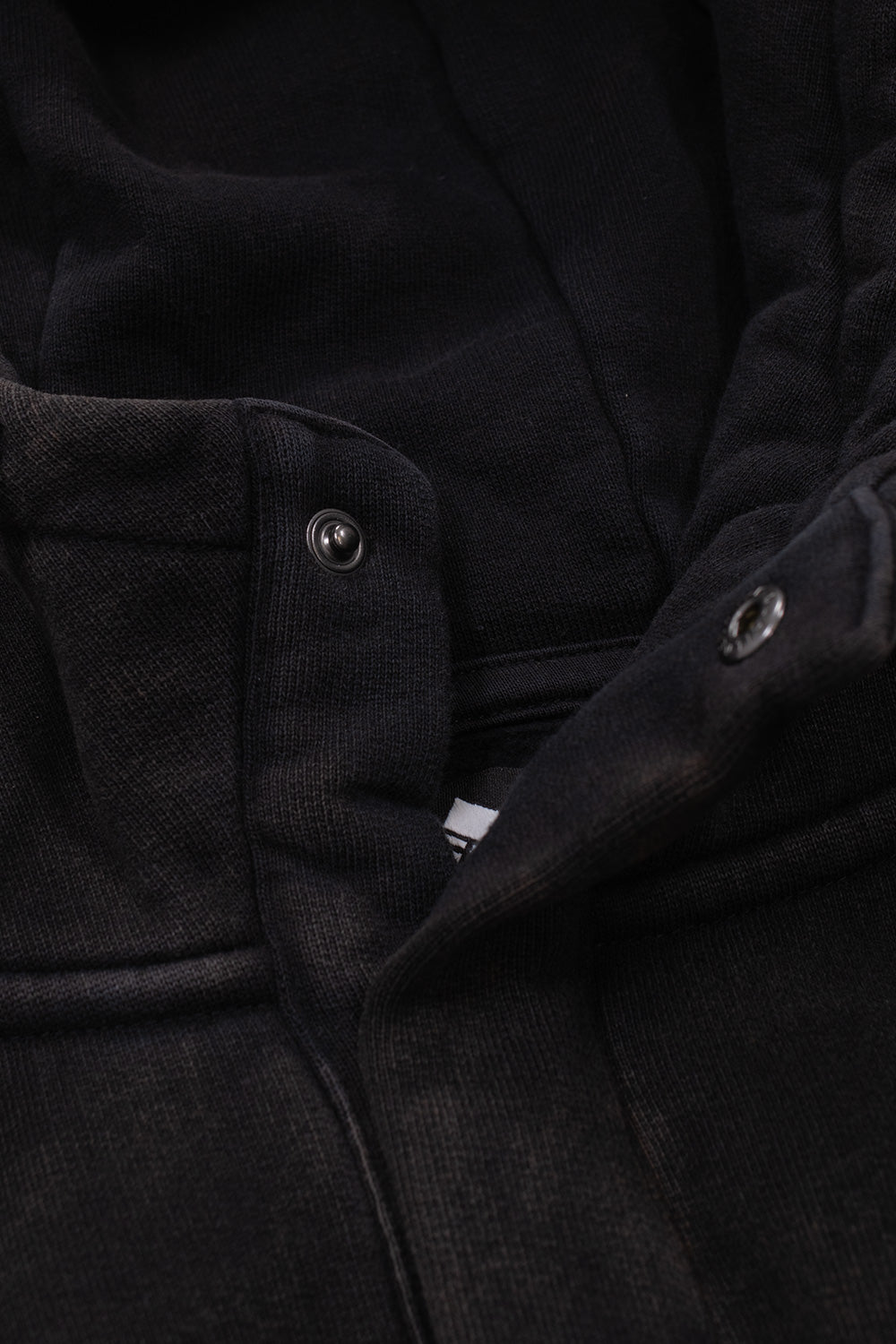 Close-up of the The Trilogy Tapes Dash Line Hood Black Acid Wash highlighting the snap fastener collar, heavyweight brushed cotton interior, premium construction details and soft fleece lining for everyday comfort.