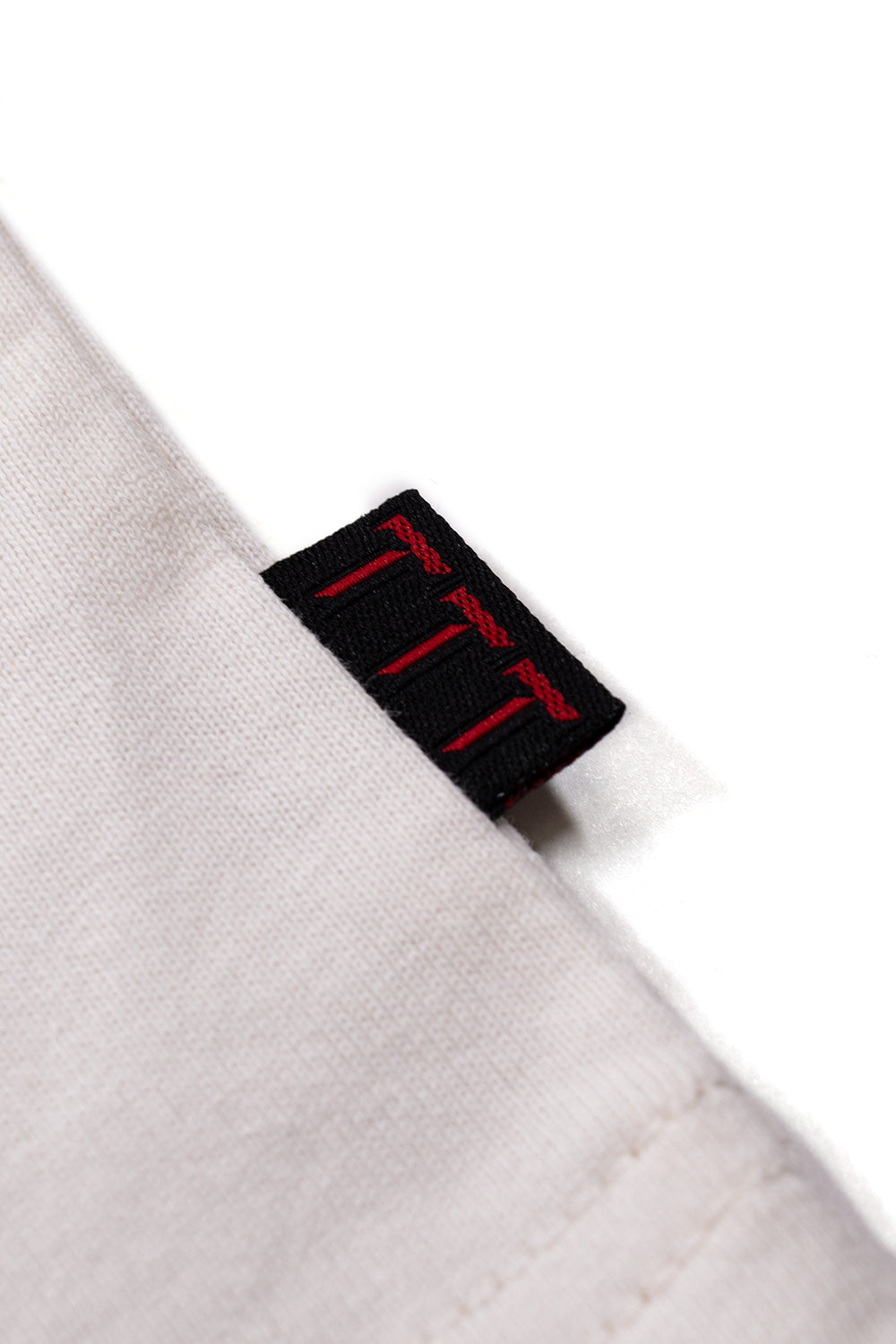 Detailed view of the woven TTT side label on the The Trilogy Tapes Double Headed Longsleeve White, highlighting premium 100% cotton construction, refined garment finishing, loose-fitting silhouette and authentic contemporary streetwear craftsmanship.