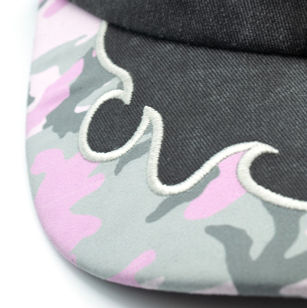 Macro studio view of the visor transition on the Token Bae Cap, focusing on the dense white embroidered flame-edge appliqué border joining the faded black crown to the pink, grey, and white camouflage printed twill brim.