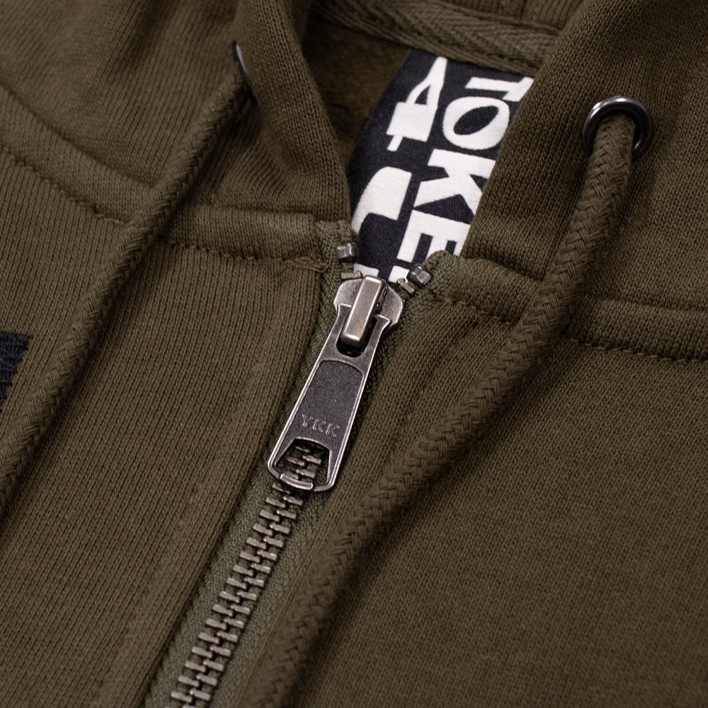 Detailed macro studio close-up of the neckline and zipper closure on the Token Carly Zip Hoodie, highlighting the antique silver metallic YKK zipper pull, metal hood eyelets with round drawstrings, and the black-and-white woven "TOKEN 4U" interior collar tag.