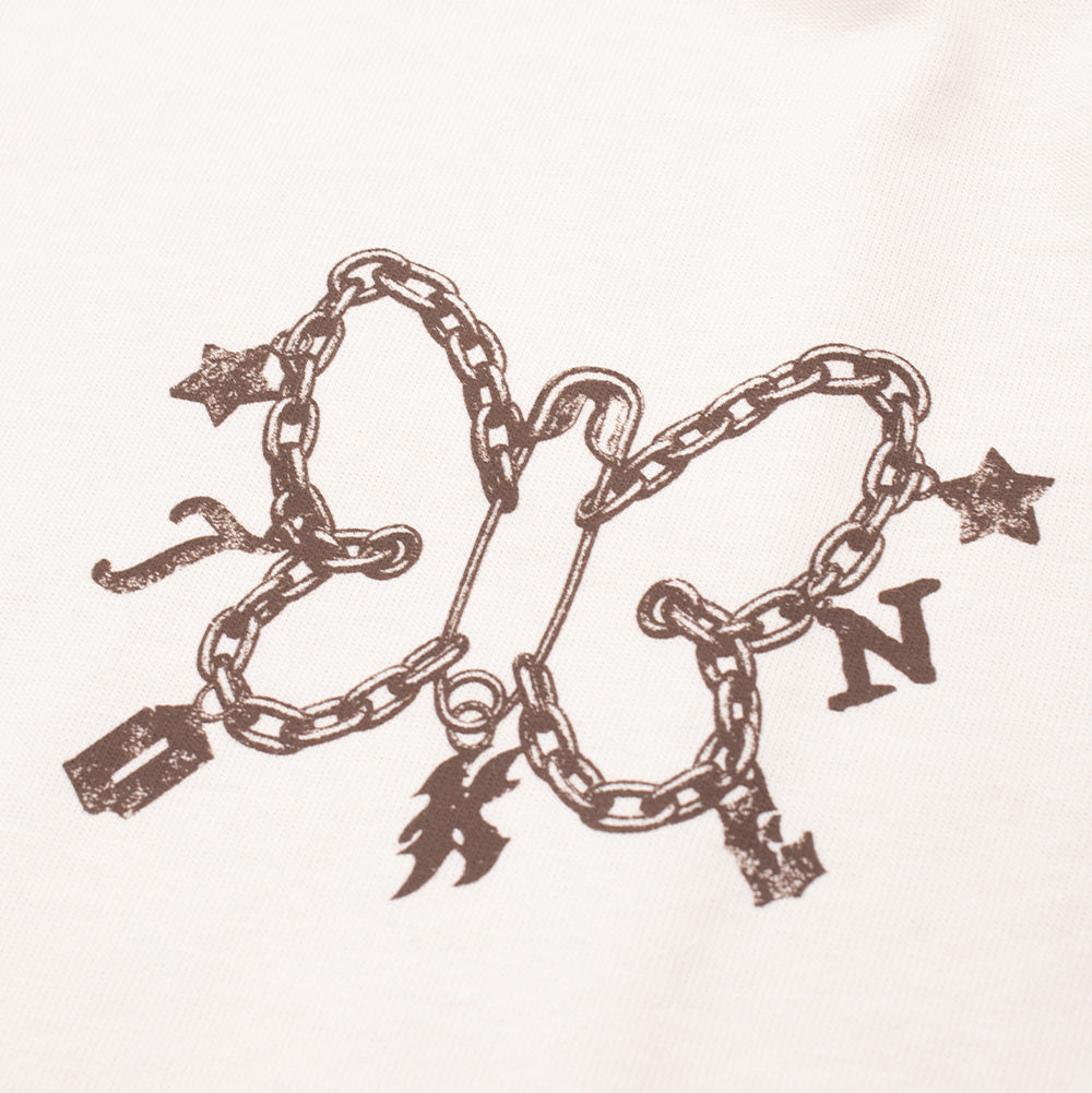 Macro studio close-up of the front graphic on the Token Expansive Skies T-Shirt, highlighting the intricate brown screen print featuring a butterfly silhouette created with link chains, hanging razor blade and star charms, gothic "TOKEN" letter charms, and a detailed center safety pin on light cotton fabric.