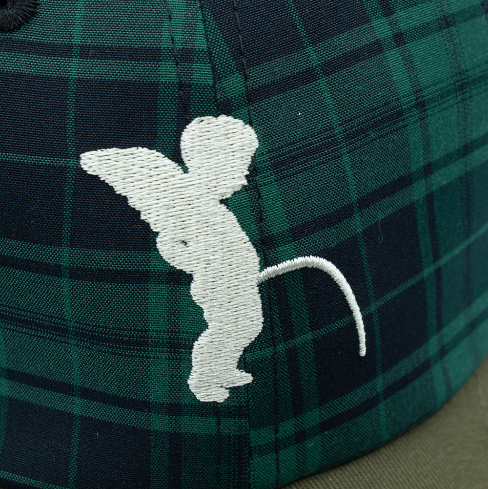Detailed macro studio close-up of the front panel on the Token Pissing Angel Cap, highlighting the dense white embroidery depicting the winged Manneken Pis cherub statue, set against the rich woven green, dark navy, and black Scottish tartan plaid fabric weave.