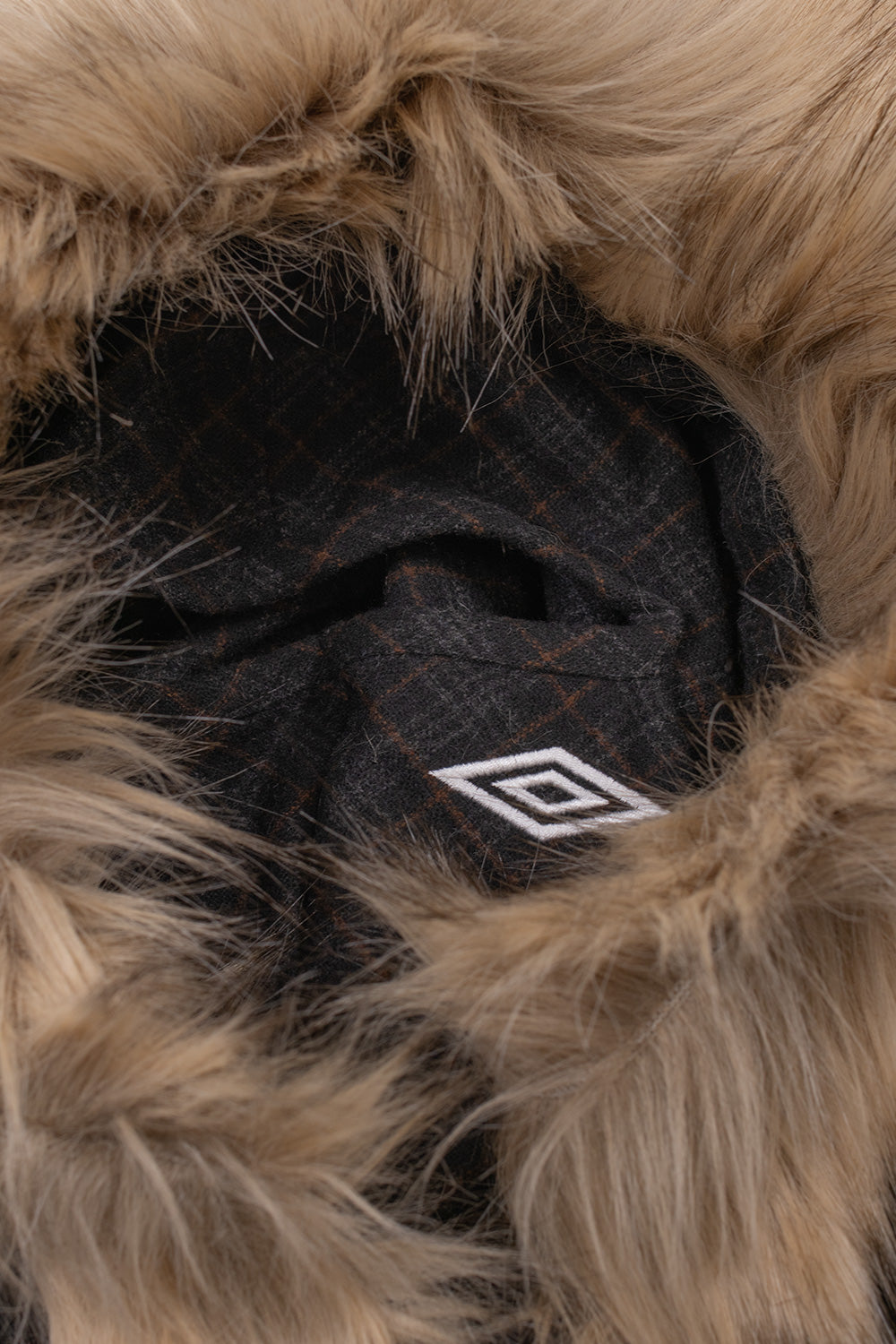 Macro close-up perspective of the hood opening on the Umbro Flannel Fur Anorak, showcasing the dense, soft faux fur trim framing the face alongside the inner plaid lining and the embroidered white Umbro diamond branding