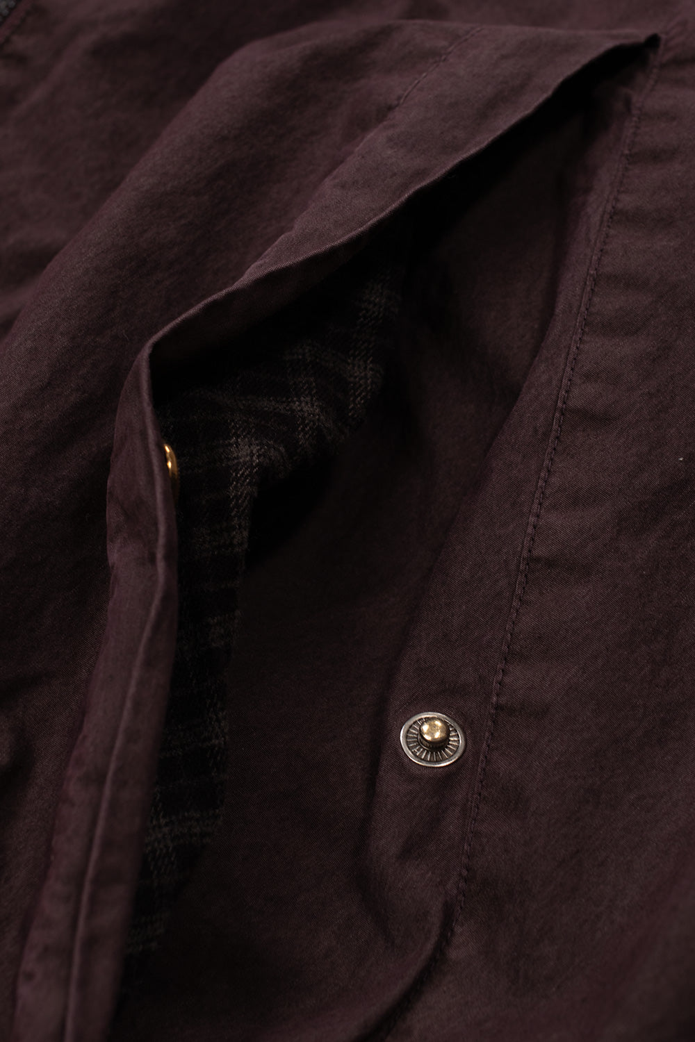 Close-up shot of the open slanted hand pocket on the Umbro Sunday Masked Jacket, showing the metallic engraved snap button closure, neat topstitching, and a glimpse of the internal brown tartan check lining