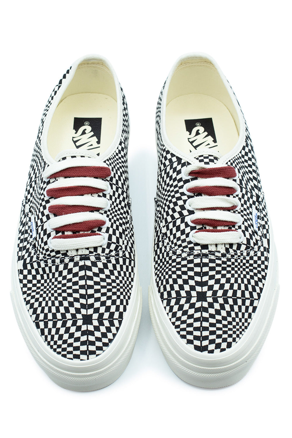 Top-down perspective of a pair of Vans LX Authentic 44 Heritage Black low-top shoes, highlighting the eye-catching warped checkerboard pattern across the canvas toe box, red and white cotton laces through silver metal eyelets, and cream insoles.
