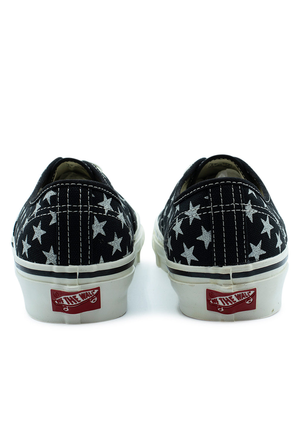Rear view of the heels of the Vans LX Authentic 44 shoes, showing the white double-stitched back seams on black star-printed canvas and the red Off The Wall rubber heel license plate patch attached to the glossy marshmallow midsole.