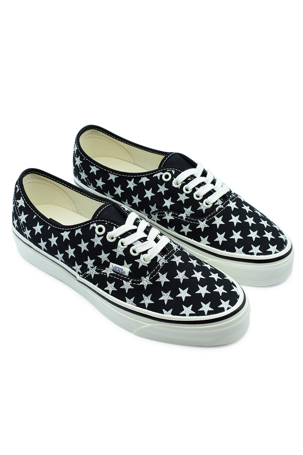 Three-quarter perspective studio view of both Vans LX Authentic 44 (Stars) Black / Marshmallow sneakers, highlighting the low-slung 90s silhouette, retro Osnaburg foxing tape texture, and the woven Vans flag tag on the lateral side seam.