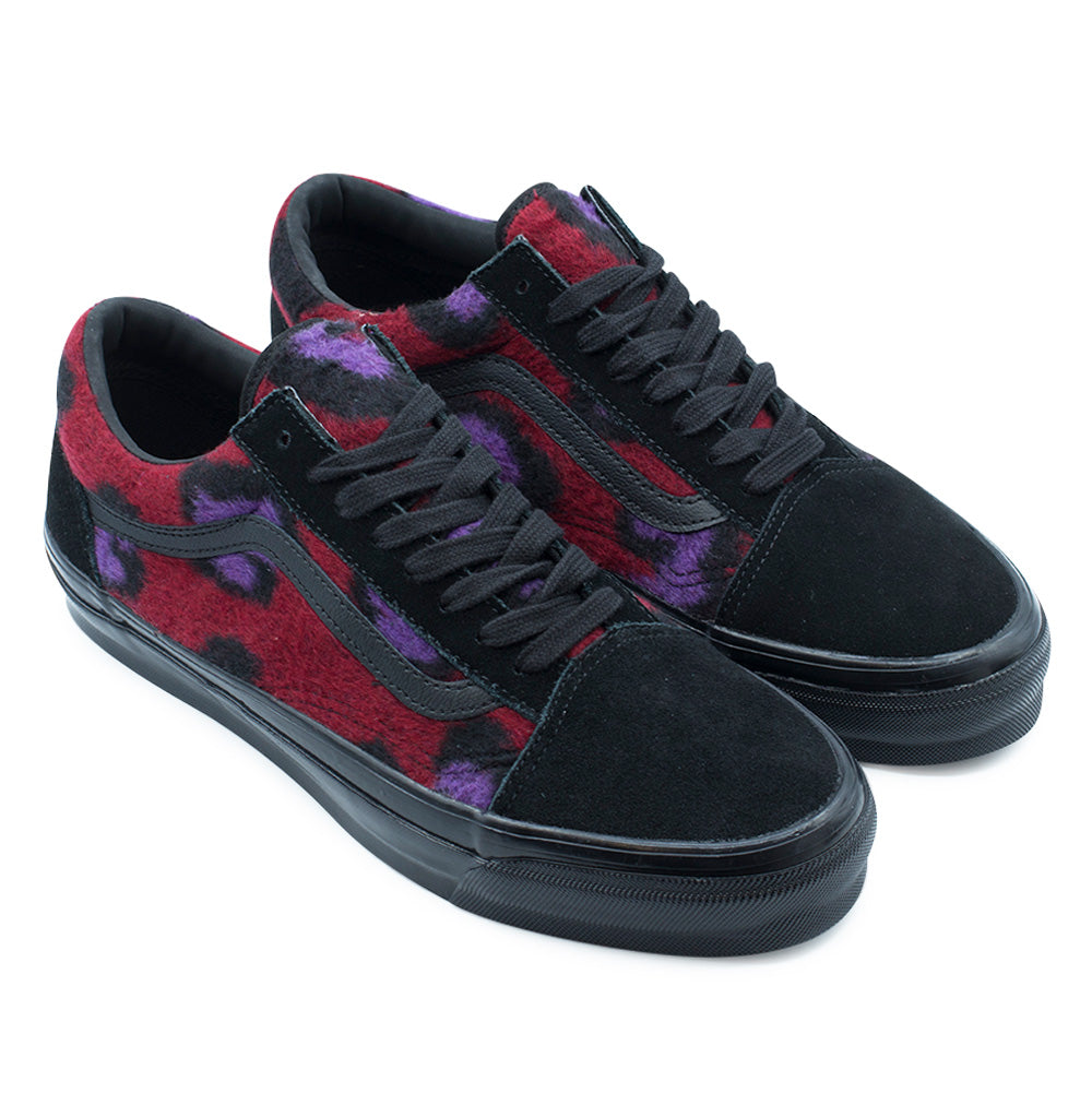 Three-quarter studio view of the Vans LX Old Skool in Leopard Black / Multi, highlighting the clash of textures between the smooth black suede front, shaggy red-purple-black leopard fleece side panels, stitched leather sidestripes, and tonal black rubber midsoles.