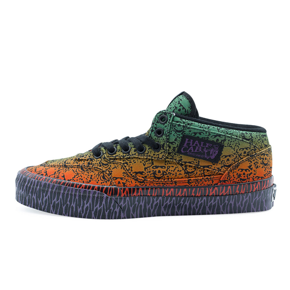 Lateral profile studio view of the Vans OTW x Chito Half Cab 33 shoe in Skull, showcasing the classic mid-top skate silhouette crafted from heavy canvas with an ombre airbrush-style gradient fading from radioactive green at the collar down to bright orange and red, completely overlaid with Chito's intricate black skull illustration, finished with a purple embroidered Half Cab ankle patch and glossy black vulcanized foxing tape printed with red and purple tribal line graphics.