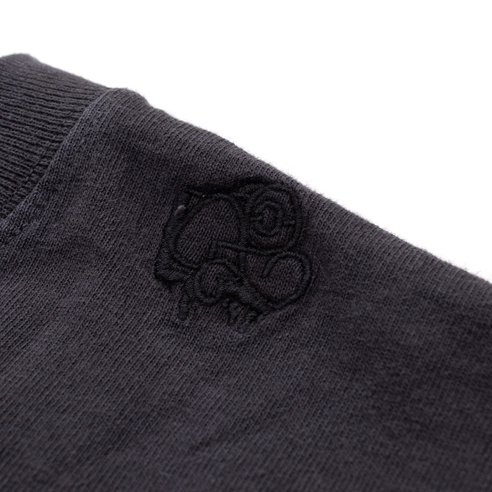 Macro studio close-up of the left collar shoulder seam on the Vans OTW x Chito T-Shirt, displaying the subtle tonal black satin embroidery depicting Chito's signature stylized cartoon dog motif stitched directly beside the ribbed neckline.