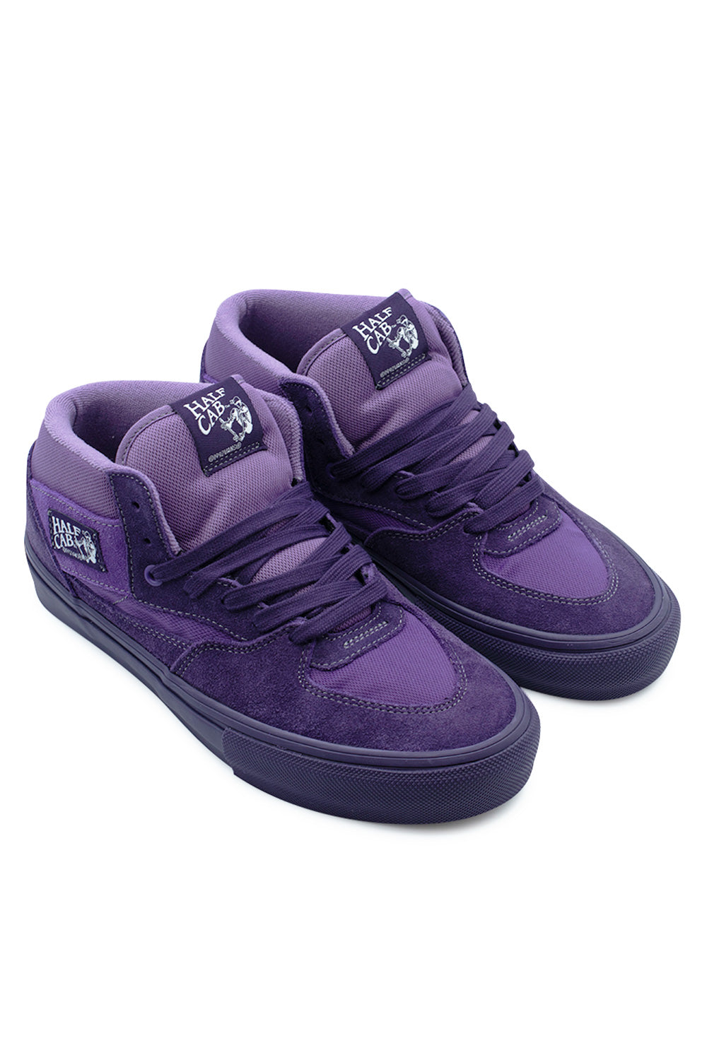 Elevated three-quarter studio shot of the Vans Skate Half Cab shoes in Purple Licorice, illustrating the mid-top silhouette, impact-absorbing PopCush drop-in footbeds, tonal purple stitching, and side panel heritage patches.