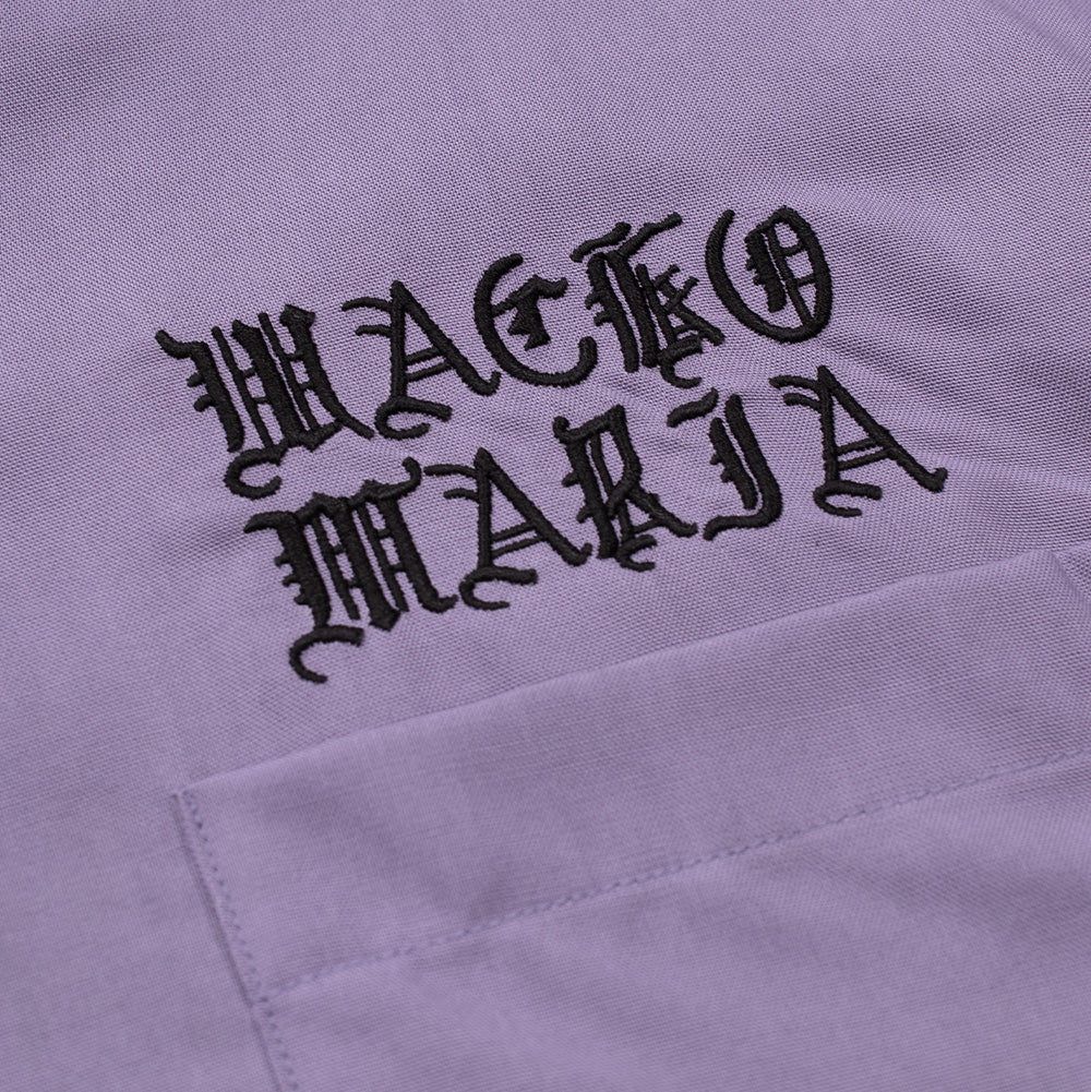 Detailed macro perspective of the chest embroidery on the Wacko Maria 50's Shirt, showcasing the dense black satin-stitch thread forming the two-tiered Old English gothic "WACKO MARIA" lettering positioned precisely above the seam of the chest patch pocket.