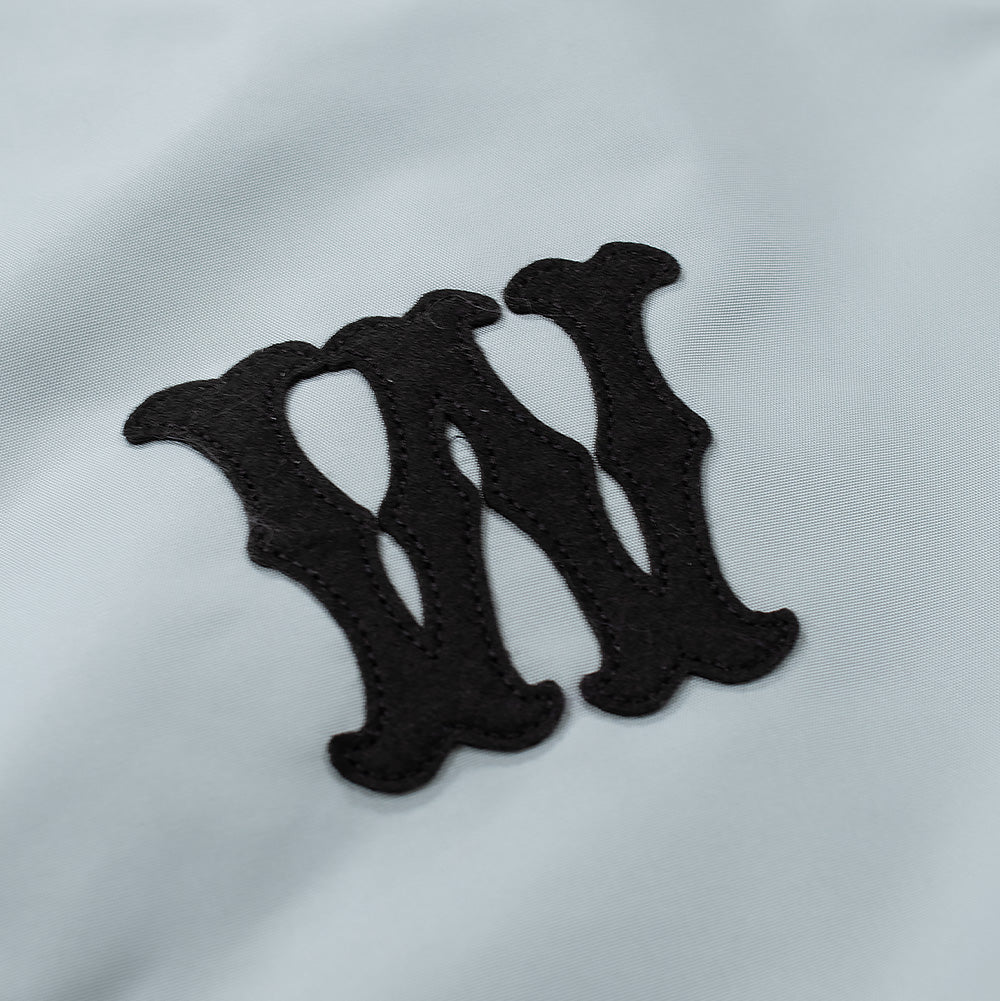 Detailed macro perspective of the chest embroidery on the Wacko Maria Coach Jacket, highlighting the dense black felt letter "W" in stylized western gothic typography securely stitched onto the pale grey fabric with matching black border embroidery.