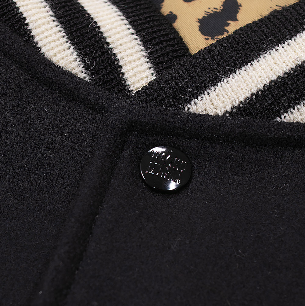Macro close-up shot of the collar construction and upper snap button on the Wacko Maria Leather Varsity Jacket, detailing the black and off-white striped ribbed knit trim, dense black wool melton fabric, branded glossy black metal snap button, and the leopard pattern inner lining.