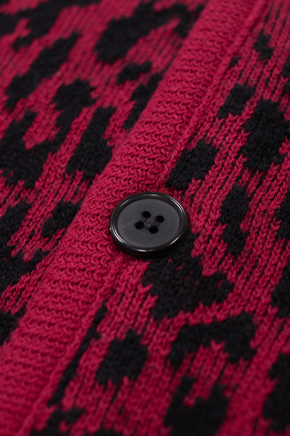 macro detail of black button closure on Wacko Maria leopard jacquard cardigan, textured knit fabric with bold red and black animal pattern