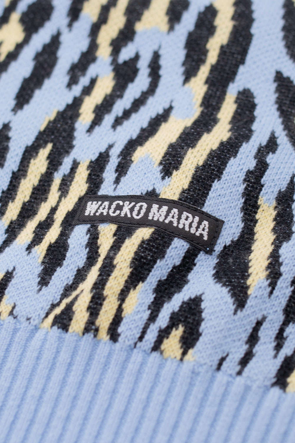 Detailed view of woven leopard jacquard pattern on Wacko Maria sweater in light blue with signature side label, breathable cotton knit texture, premium Tokyo street fashion piece