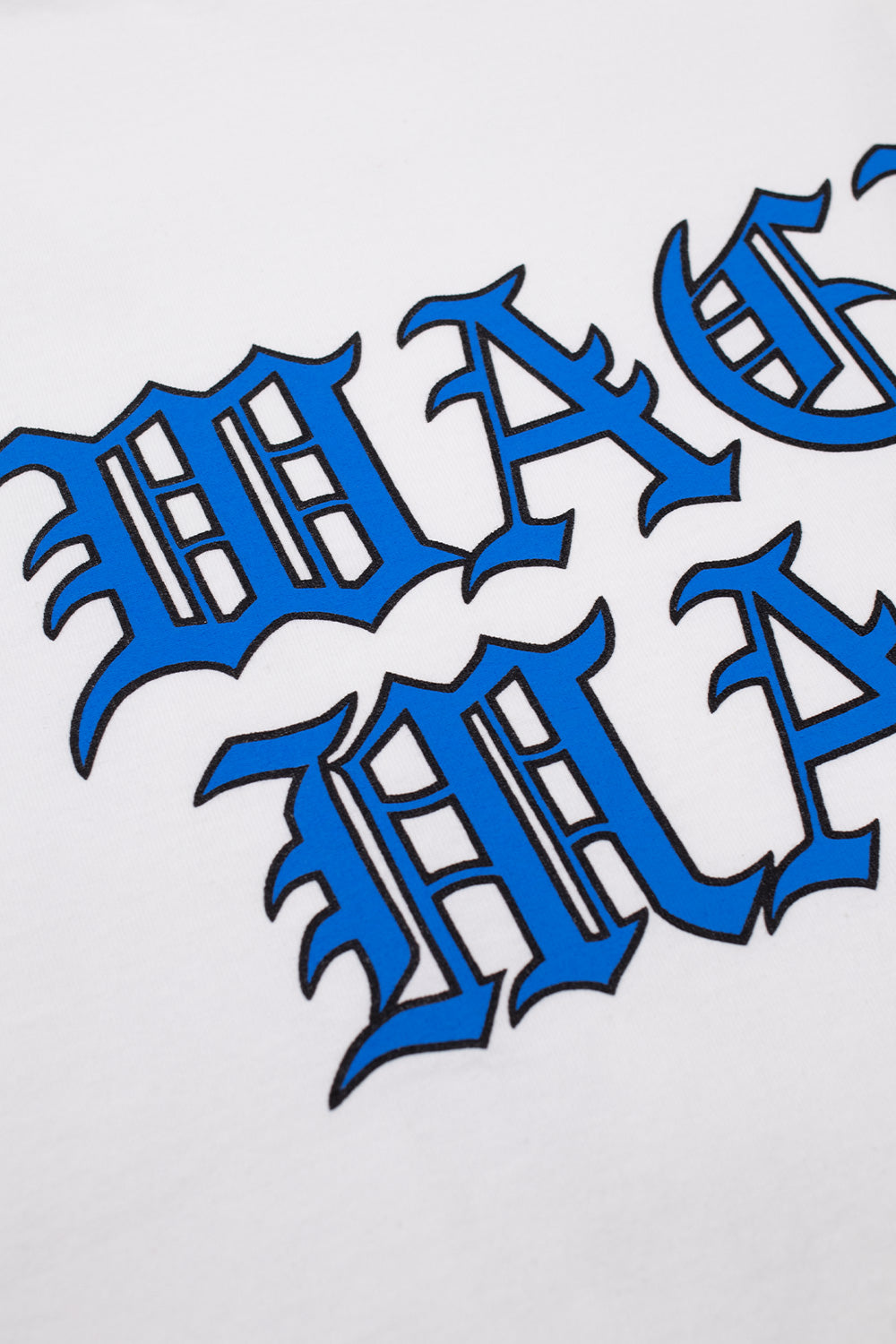 Close-up detail of the blue and black Gothic font logo printed on the chest of the white Wacko Maria heavy weight cotton t-shirt.