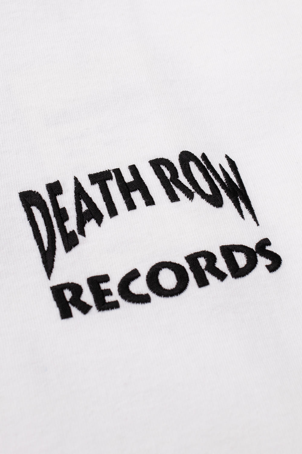 Detailed macro shot of the black embroidered Death Row Records arched logo on the chest of the white t-shirt.