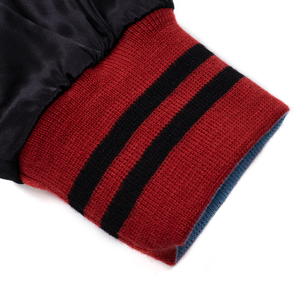 Close-up studio perspective of the reversible sleeve cuff on the Wacko Maria x True Romance Ska Jacket, displaying the rich red rib-knit cuff with two horizontal black stripes on the outside and light blue ribbed lining folded beneath the black satin sleeve.