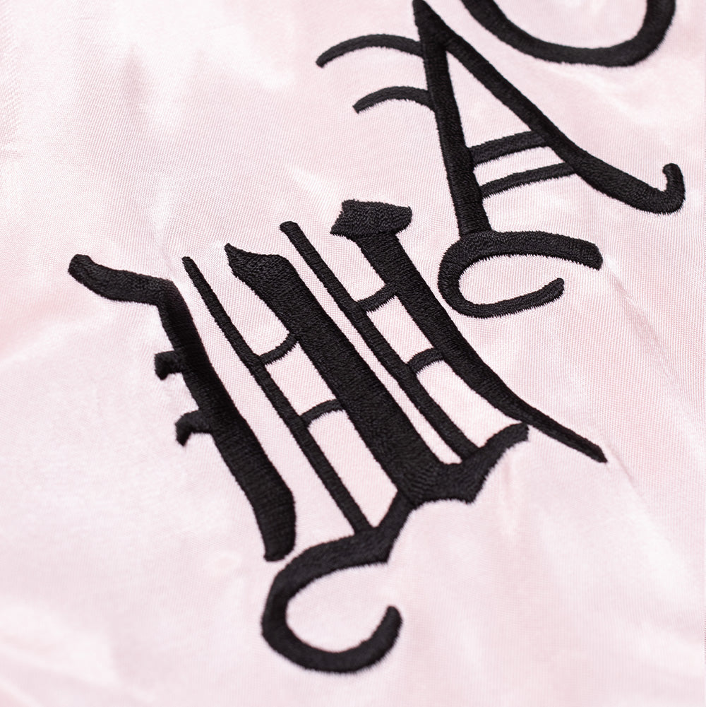 Extreme macro close-up of the rear embroidery on the pink satin side of the Wacko Maria x True Romance Ska Jacket, showcasing the dense, high-precision black satin-stitch embroidery forming the letters "WA" from the brand's signature Old English gothic typography against the shimmering blush pink textile weave.