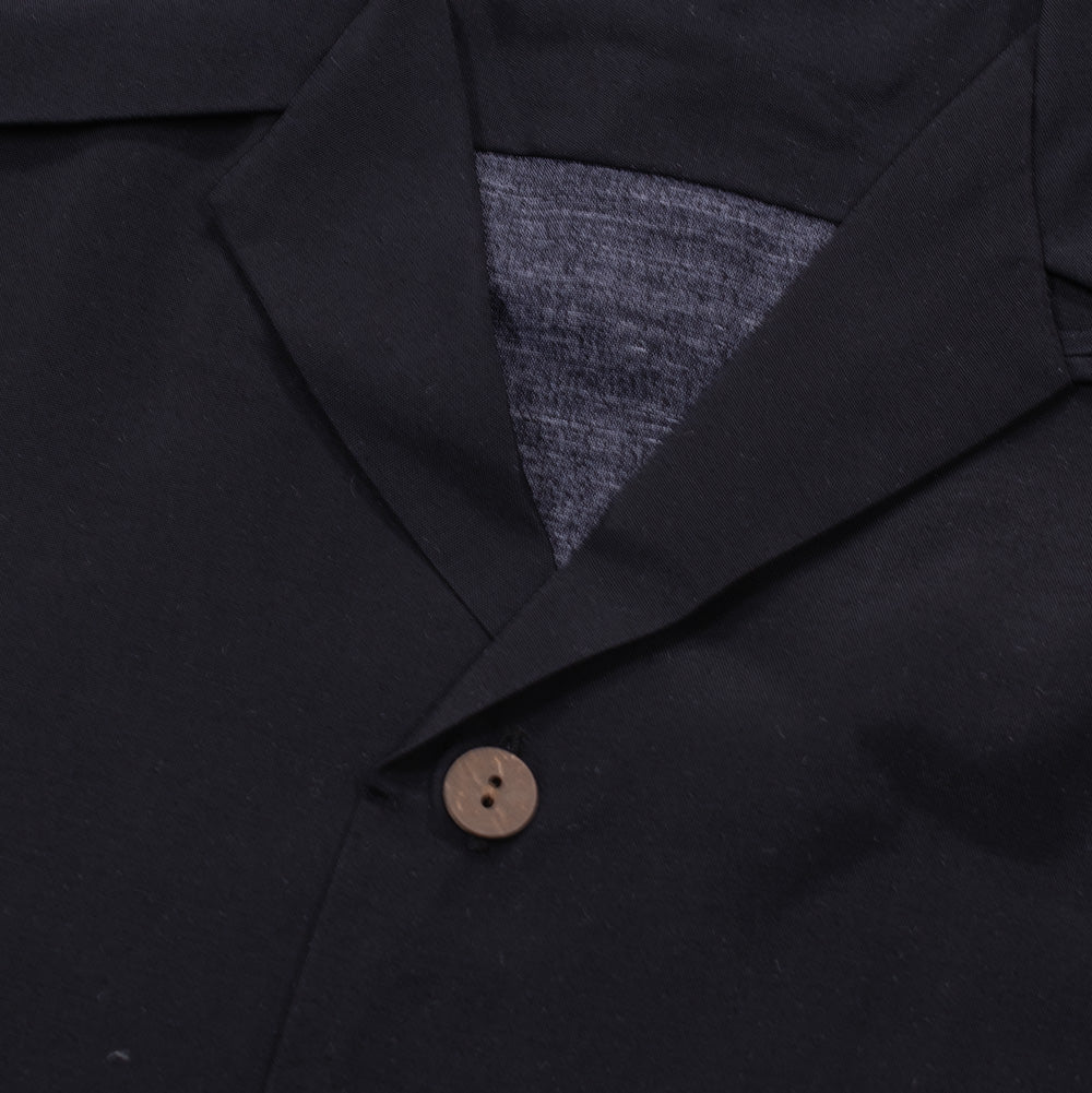 Macro studio close-up of the open Cuban camp collar and top button on the Wacko Maria x True Romance Hawaiian Shirt, displaying the textured charcoal inner back yoke lining and the circular carved brown coconut-style button set against lightweight black woven fabric.