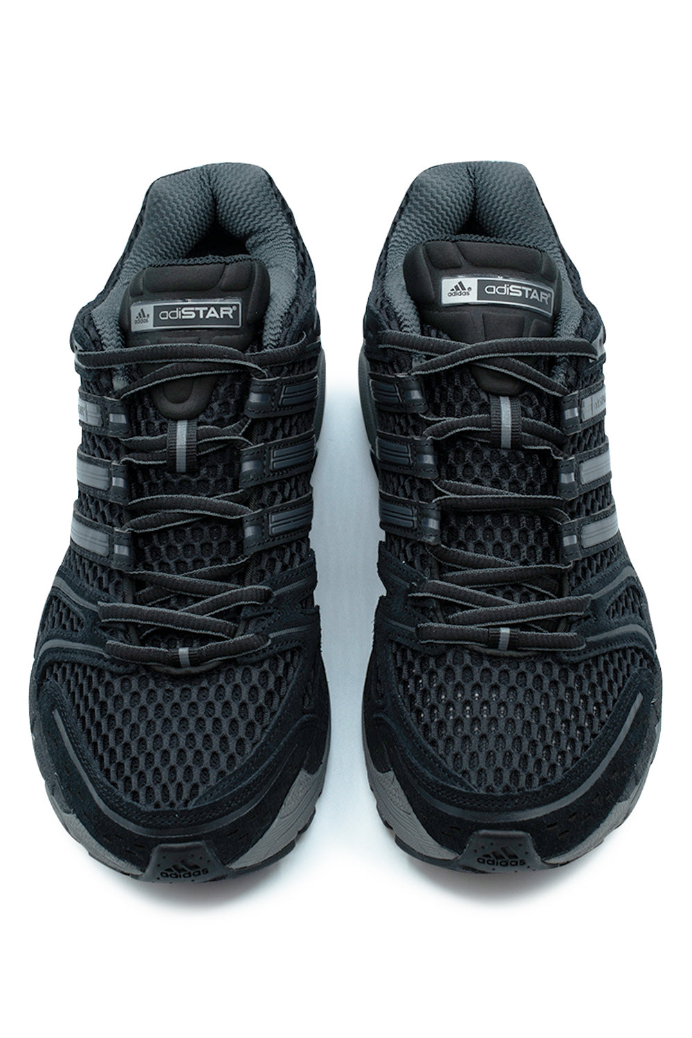 Top-down view of a pair of Adidas Adistar Control 5 shoes in Core Black, displaying the wide honeycomb mesh forefoot, reinforced suede toe caps, black ghillie lacing system, and padded mesh tongues with white and silver adiSTAR logo branding patches.