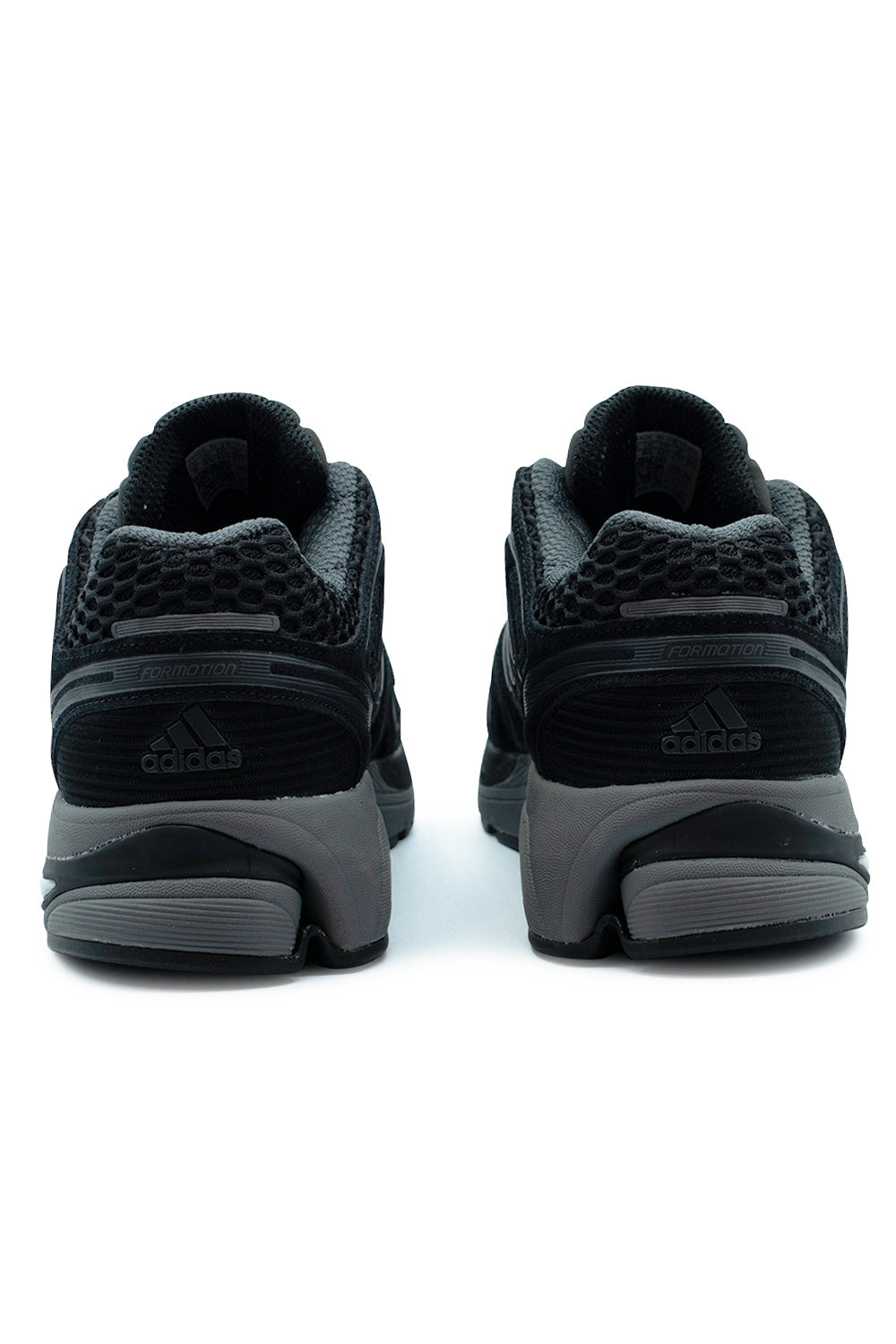 Rear view of the heels of the Adidas Adistar Control 5 sneakers in Core Black / Grey Six, showing the breathable wide mesh collars, horizontal Formotion suspension heel unit, and debossed Adidas Badge of Sport mountain logos on the ribbed heel counters.