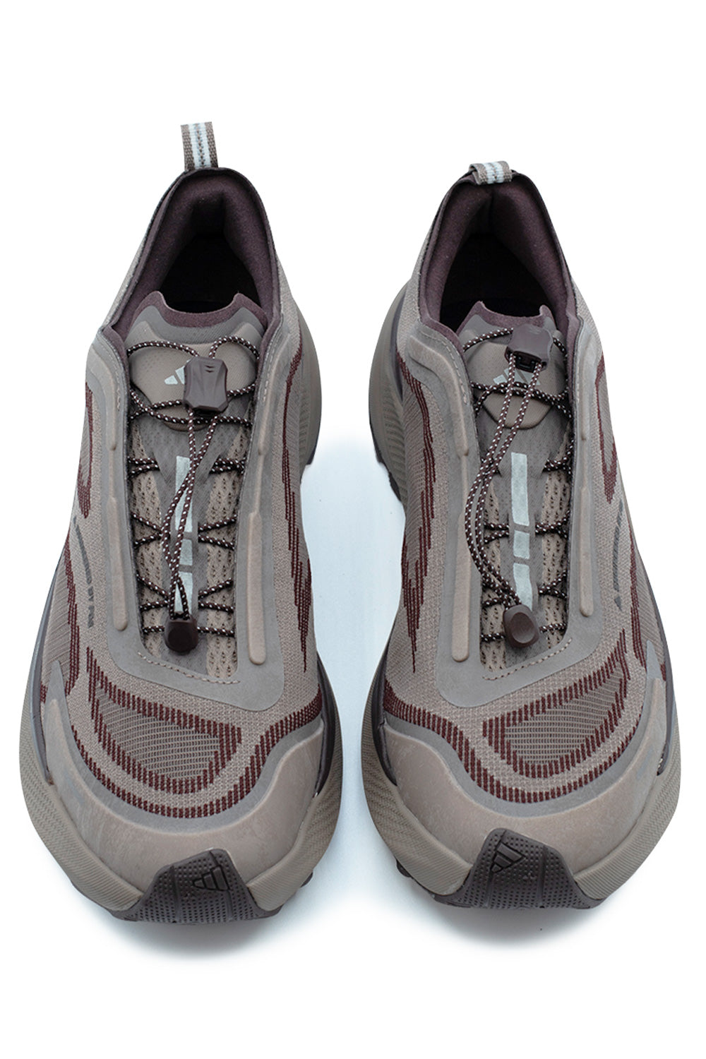 Top-down view of a pair of Adidas Holo Peak shoes in Trace Brown, highlighting the elastic quick-pull speed lacing toggle system, brown synthetic mudguard overlays, perforated mesh tongue with Adidas mountain logo, and striped pull loops.