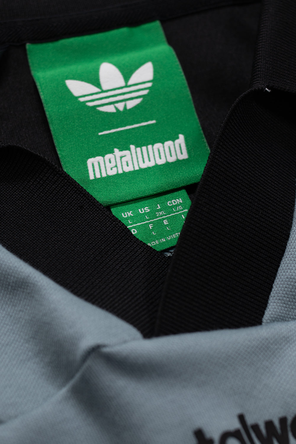 Close-up of adidas x Metalwood Polo Green Earth collar showing collaborative adidas Originals and Metalwood Studio branding, premium stitching and breathable lightweight performance fabric