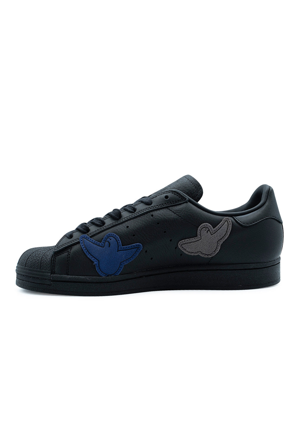Medial inner arch view of the Adidas Superstar ADV Gonz sneaker, showing the solid black leather quarter panel detailed with diagonal perforated 3-Stripes, an applied royal blue suede Shmoo ghost patch near the forefoot, and a light grey Shmoo patch near the heel.