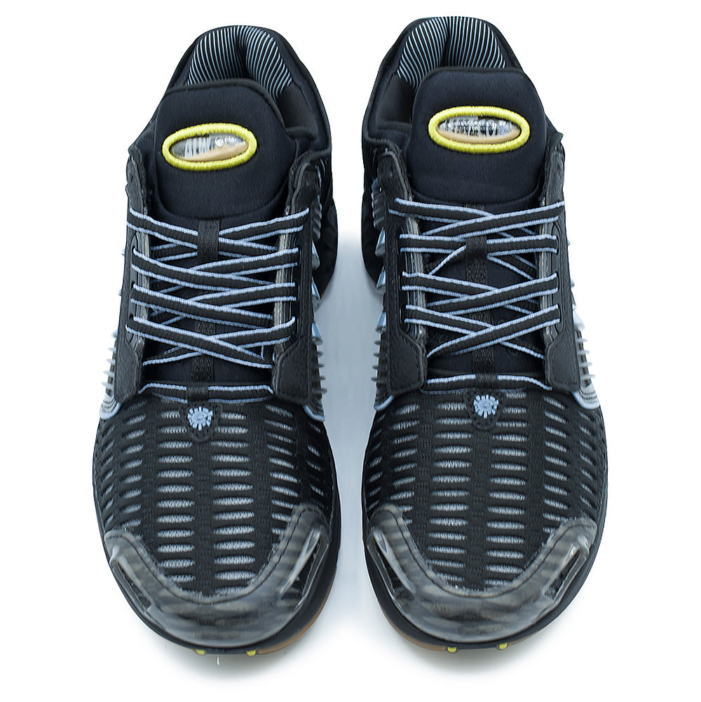 Top-down studio shot of the adidas x ADWYSD Climacool 1 pair, highlighting the ribbed high-airflow forefoot mesh, thin black and white flecked laces through floating eyestays, translucent TPU protective toe caps, and padded black neoprene tongues fitted with oval liquid badges containing real sand and floating branding inside a yellow embroidered border.