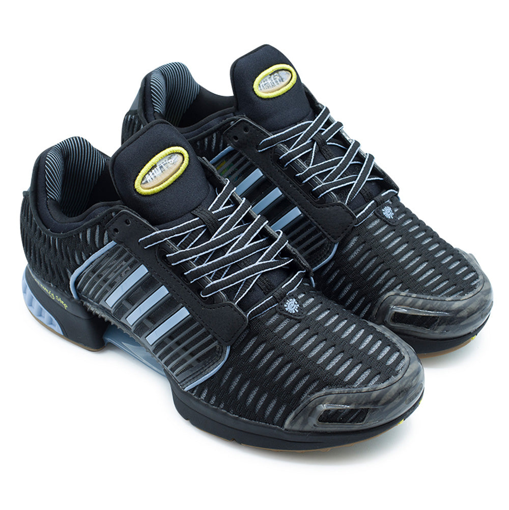 Three-quarter studio view of the adidas x ADWYSD Climacool 1 sneakers, showing the low-top Y2K retro runner construction, translucent caged TPU midfoot sidewalls with light blue three stripes, structured transparent toe overlays, and the sand-filled novelty tongue emblems framed by neon yellow thread.