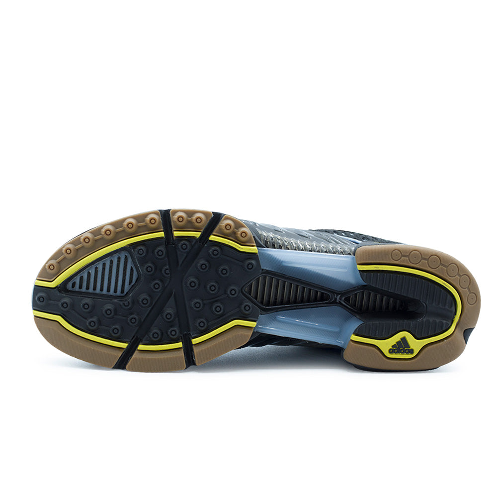 Full bottom studio flat lay of the adidas x ADWYSD Climacool 1 decoupled rubber outsole, displaying circular suction lugs, transparent blue midfoot ventilation tunnels with inner mesh grilles, gum rubber borders, and bright yellow contrast perimeter lines around the forefoot and heel.