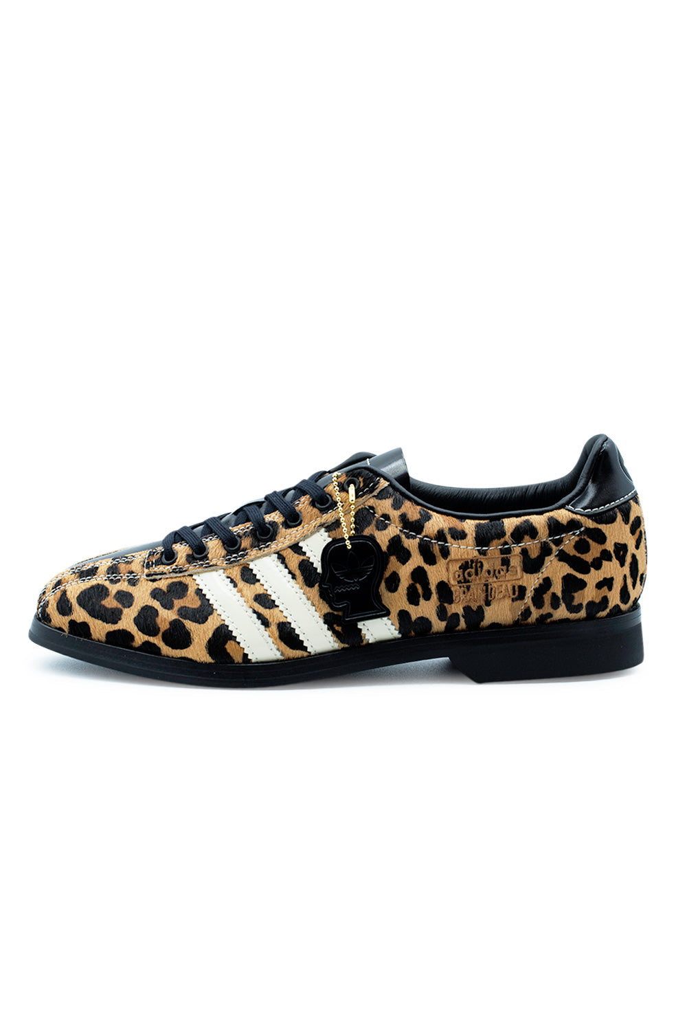Lateral profile view of the Adidas X Brain Dead Bowling shoe, showcasing the tactile printed cheetah leopard pony hair upper, off-white serrated Three Stripes, flat black laces, gold-foil Adidas Brain Dead lettering, hanging black metal Brain Dead head logo keychain, and a flat black rubber bowling sole with a distinct block heel.