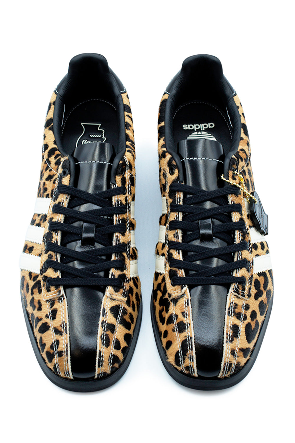 Top-down view of the Adidas X Brain Dead Bowling shoes, displaying the split-upper design combining patterned brown and black spotted cheetah pony hair sidewalls with a centered glossy black smooth leather stripe extending across the tongue and toe box, tied with flat black laces.
