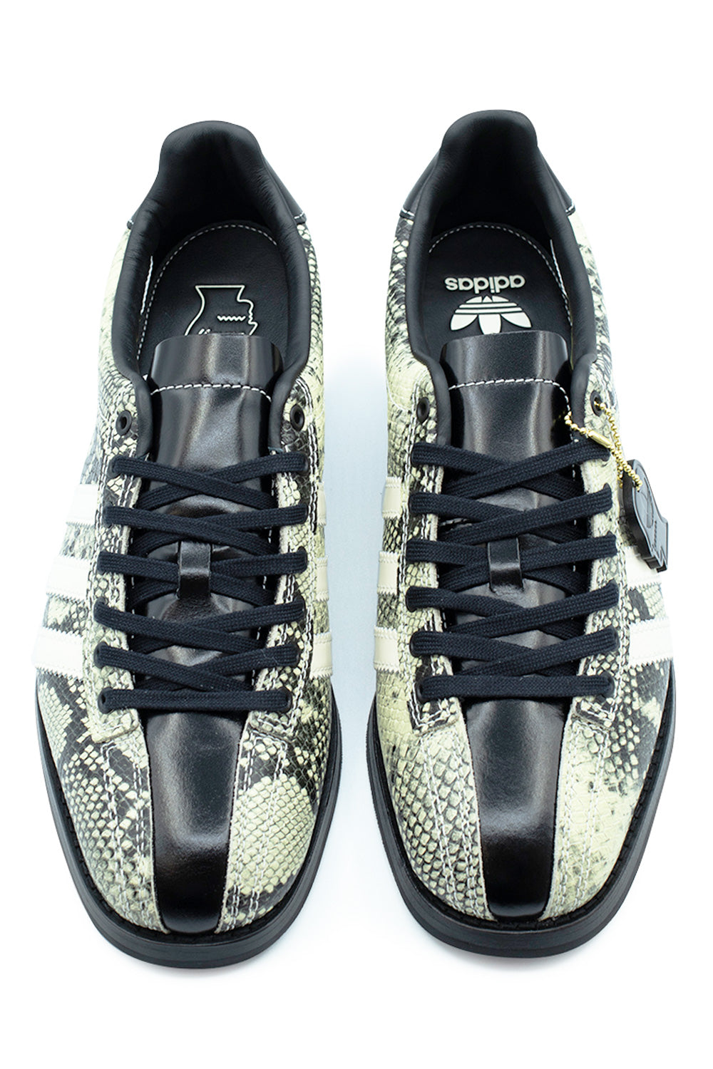 Top-down view of the Adidas X Brain Dead Bowling shoes, featuring a split-panel upper with exotic snakeskin print sides and a bold smooth black leather center stripe running down the toe box and tongue, secured with black flat laces and white contrast stitching.