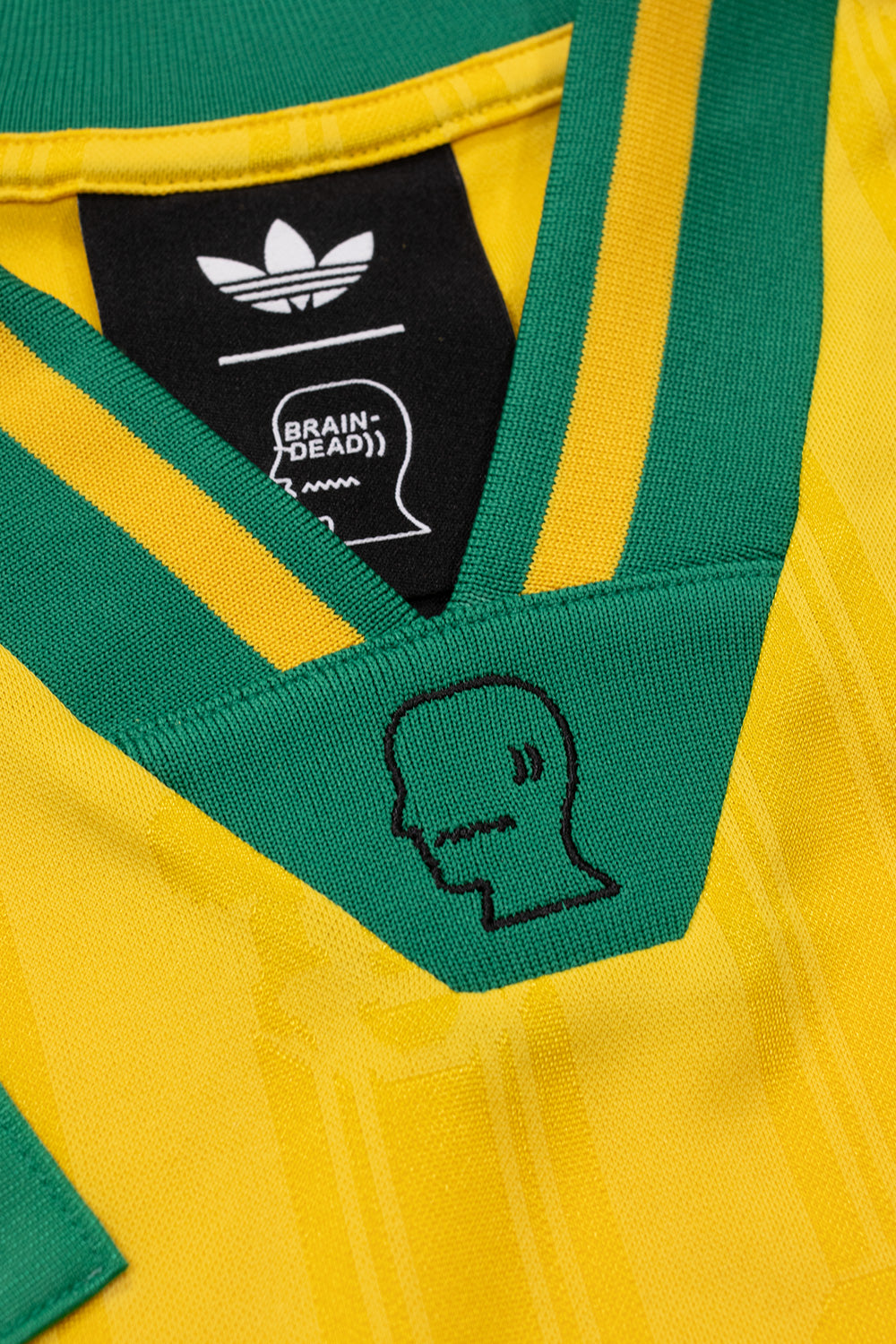 Close-up of the embroidered Brain Dead logo on the V-neck collar of the adidas x Brain Dead x Disney Football Jersey Bold Gold featuring adidas Originals branding, premium football jersey construction and retro 90s inspired design