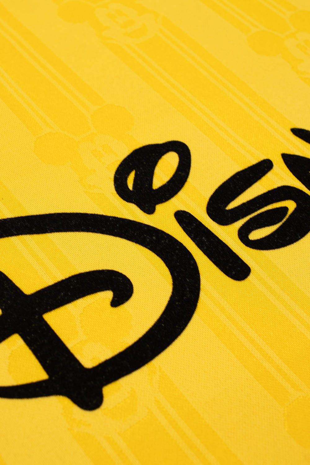 Close-up of the oversized flocked Disney lettering on the adidas x Brain Dead x Disney Football Jersey Bold Gold featuring soft velvet print, all over Mickey Mouse pattern and authentic retro football jersey design
