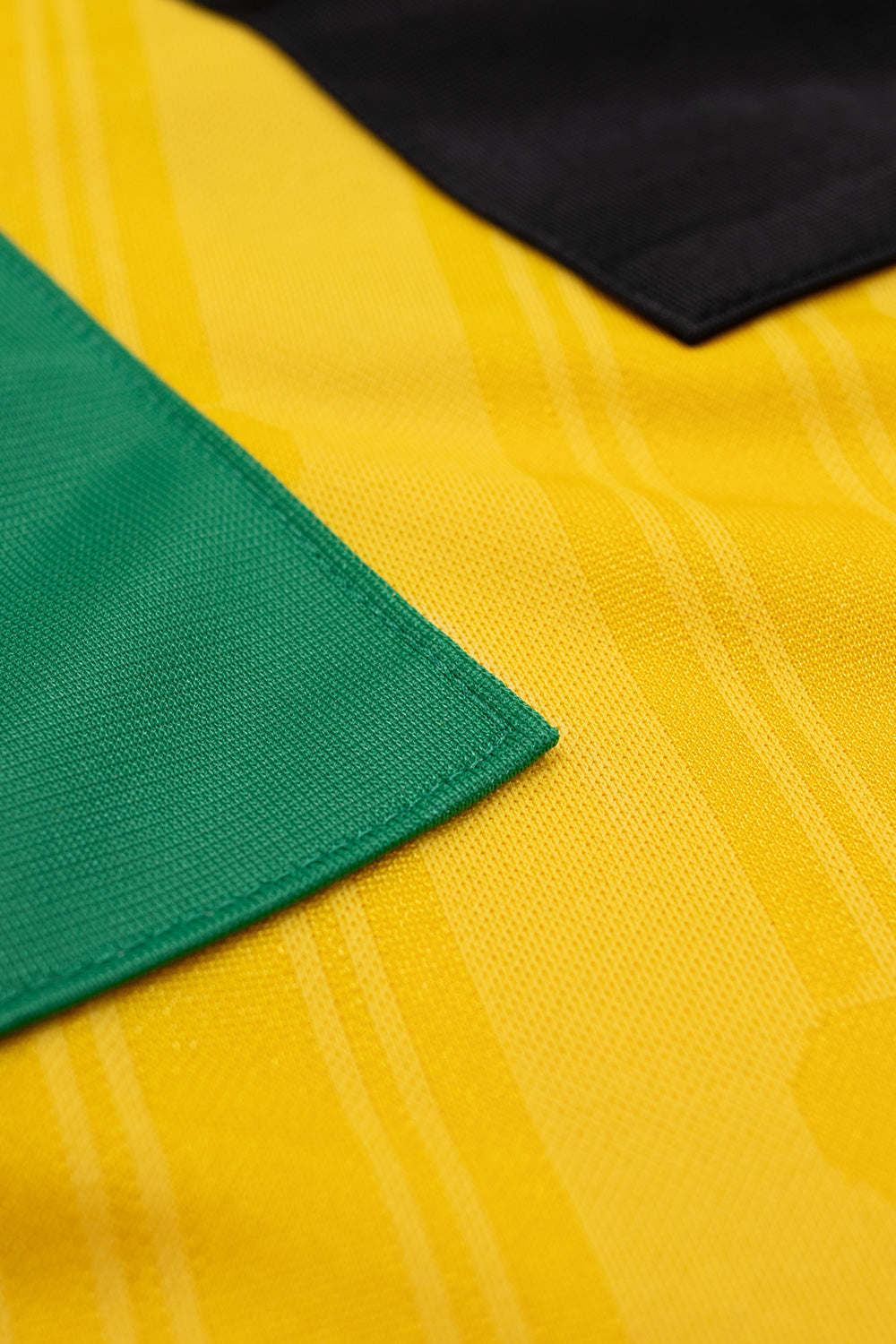 Detailed view of the sewn-on green and black adidas three stripes on the shoulder of the adidas x Brain Dead x Disney Football Jersey Bold Gold highlighting premium polyester fabric, retro football styling and limited capsule collection construction