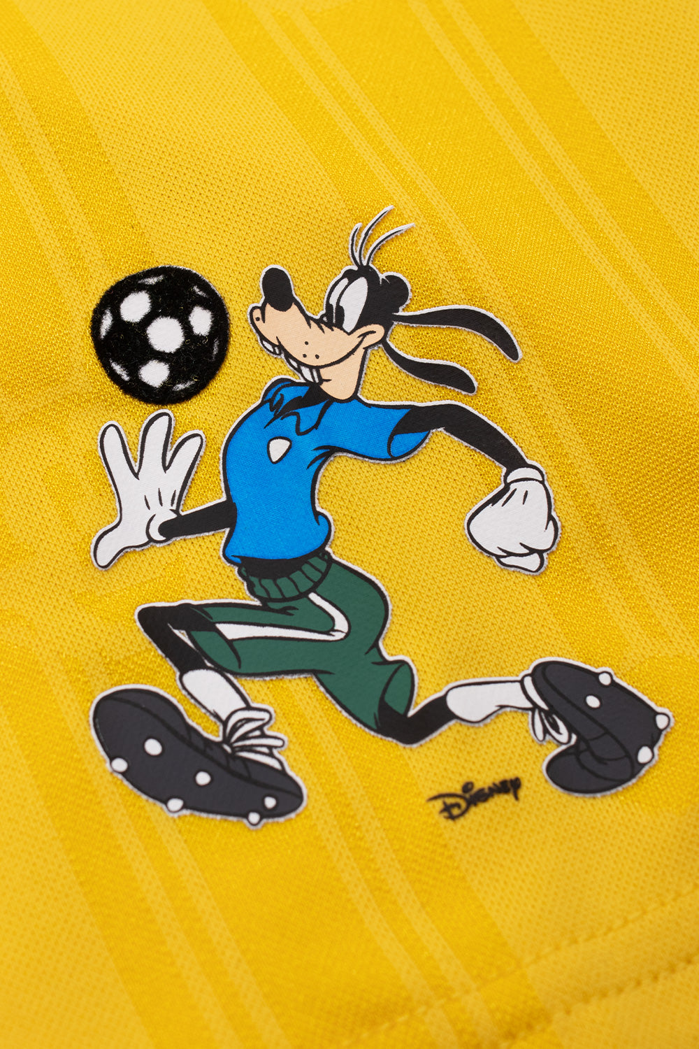 Close-up of the printed Goofy football graphic on the sleeve of the adidas x Brain Dead x Disney Football Jersey Bold Gold featuring Disney character artwork, all over Mickey Mouse pattern and exclusive World Cup capsule collection design