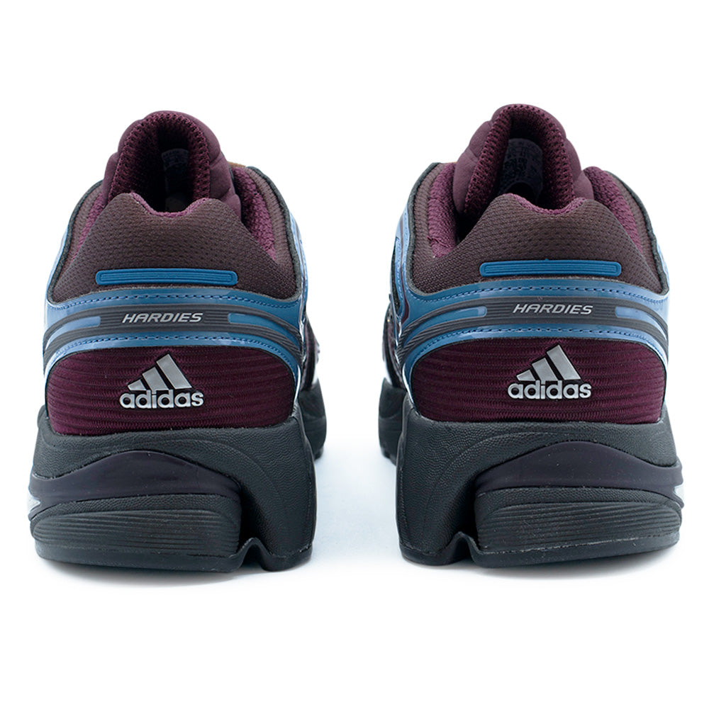 Rear heel view of the Adidas X Hardies Adistar Control 5 sneakers, highlighting the padded burgundy mesh collars, ribbed heel panels, metallic silver Adidas Performance badge logos, and slate blue TPU heel counters branded with "HARDIES" lettering.