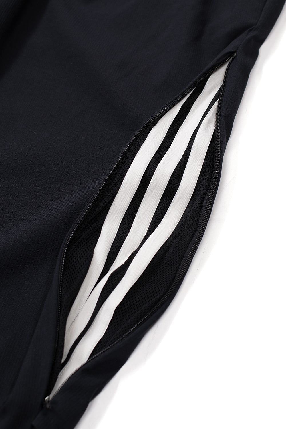 Detail of side zipper opening on Adidas x Metalwood track pants revealing breathable mesh lining and inner stripe panel, performance sports trousers ventilation feature