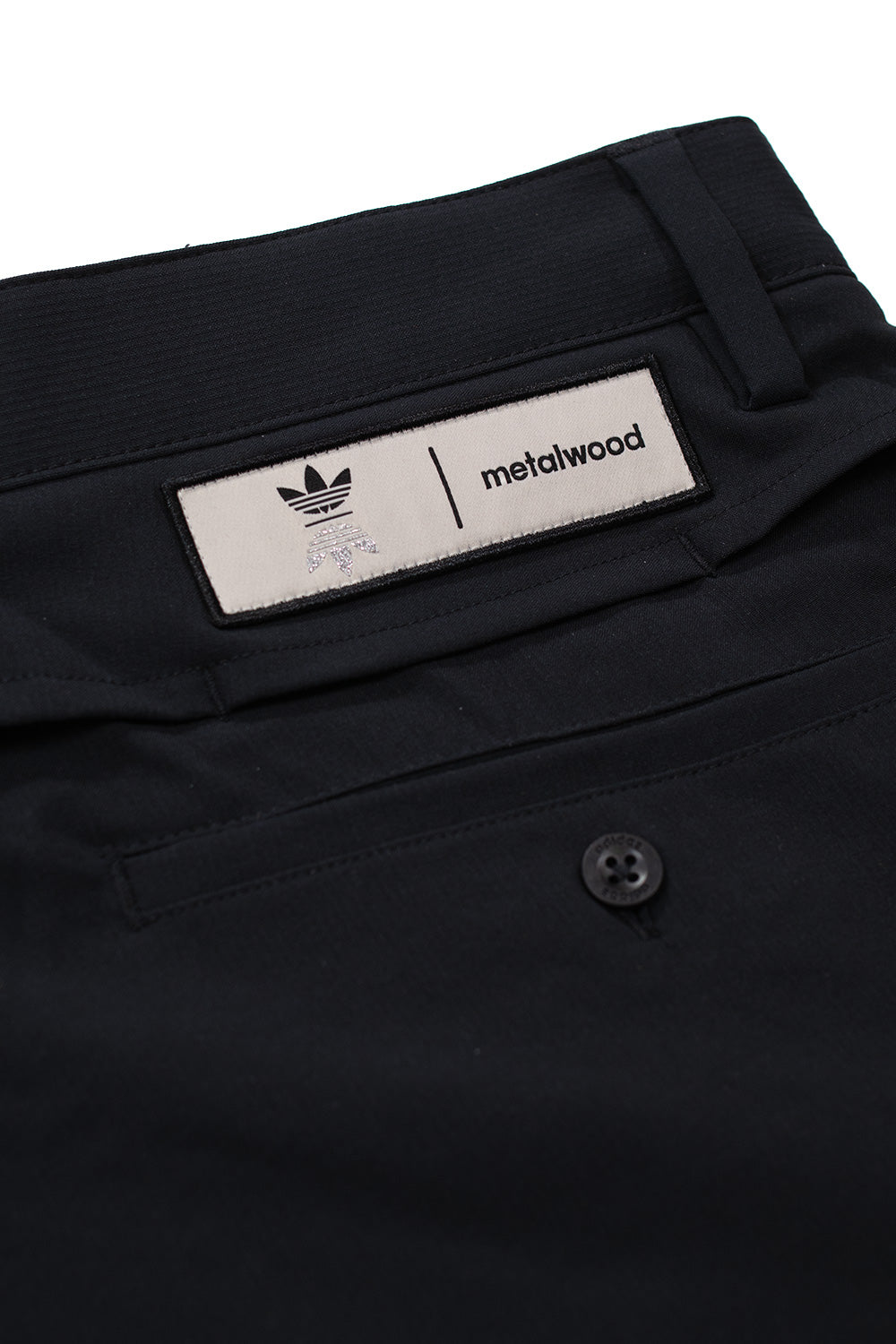 Adidas x Metalwood Studio logo patch on black tracksuit bottoms waistband, limited collaboration golf streetwear pants branding detail, modern Y2K-inspired athletic apparel
